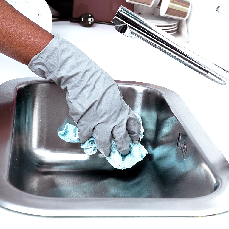 A gloved hand cleans the kitchen sink to prevent mould and mildew
