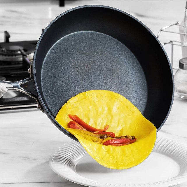 Non-stick frying pan sliding an open face omelette onto a place