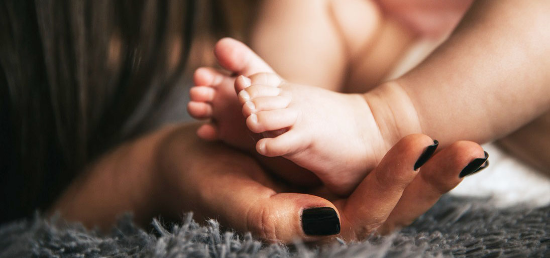 A nail polished hand cups a baby's feet